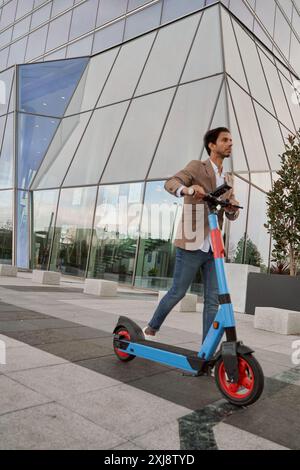 uomo d'affari indiano che cammina con il suo scooter elettrico in un quartiere finanziario. concetto di trasporto urbano ecologico Foto Stock