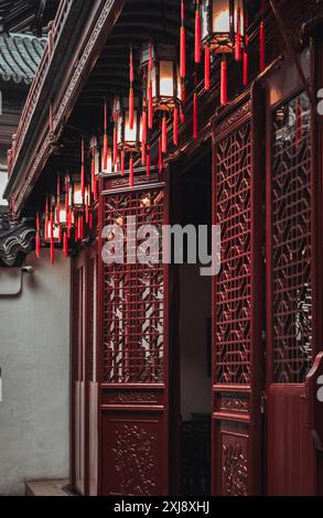 Porte di legno rosse con intricati intagli e lanterne rosse appese al soffitto di un tradizionale edificio Cinese. Foto Stock