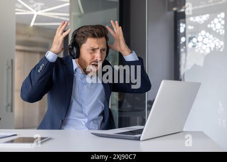 Un uomo d'affari frustrato reagisce mentre guarda una partita di sport online, mostrando confusione e delusione in un ufficio. Foto Stock