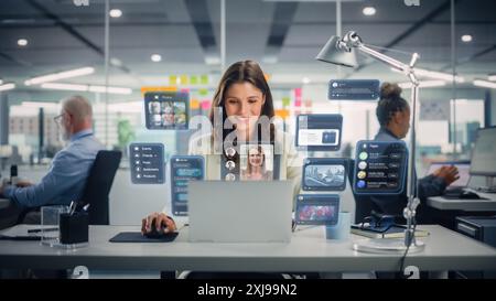 Giovane donna d'affari che utilizza un computer portatile in ufficio con i colleghi. Elegante Social Media Manager che sorride e lavora ai progetti di marketing online. Ologramma VFX Modifica visualizzazione Social Network con gli amici. Foto Stock