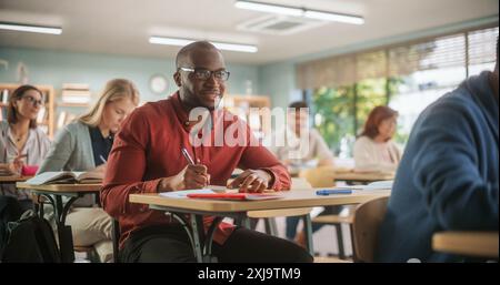 Uomo africano che scrive appunti in notebook e sorride. Gruppo di studenti maturi internazionali che studiano in classe. Il centro di formazione per adulti aiuta le persone a sviluppare nuove competenze utili per tutta la vita Foto Stock