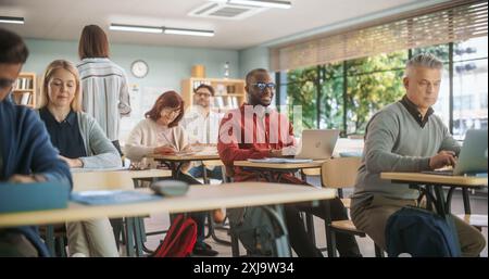 Centro di istruzione per adulti: Studenti maturi diversi che imparano in classe, utilizzano computer portatili e scrivono in notebook. Gruppo di persone che partecipano a un workshop sul miglioramento delle competenze professionali Foto Stock