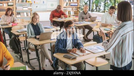 Studenti maturi diversi che imparano in aula, utilizzano notebook e scrivono notebook, acquisiscono nuove competenze. Giovane insegnante femminile che tiene una lezione durante un corso di educazione per adulti a scuola. Foto Stock