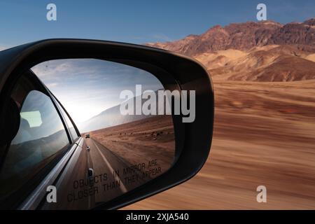 Vista dello specchio laterale di un'auto, vista della strada dietro in un paesaggio desertico del parco nazionale, paesaggio remoto e selvaggio nella Death Valley. Foto Stock