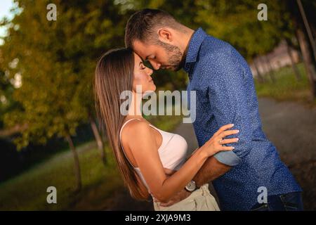 Un uomo e una donna stanno vicini in un parco al crepuscolo, con il braccio della donna intorno alla vita dell'uomo. Foto Stock