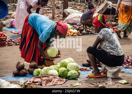 Un mercato verde aperto nell'Africa rurale ronza in una giornata di pioggia, mentre un cliente sceglie di acquistare il cavolo, circondato da molte persone sul mercato Foto Stock