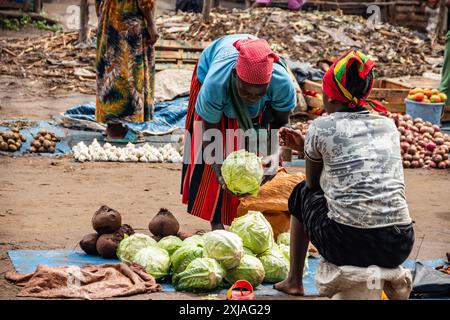 Un mercato verde aperto nell'Africa rurale ronza in una giornata di pioggia, mentre un cliente sceglie di acquistare il cavolo, circondato da molte persone sul mercato Foto Stock