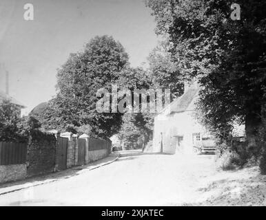 Strada non identificata con un cottage con tetto di paglia, alberi e una prima auto parzialmente nascosta, che si crede si trovi a Teignmouth, Devon. Questa fotografia proviene da un originale edoardiano, intorno al 1910. L'originale faceva parte di un album di 150 fotografie di albume, di qualità variabile, molte delle quali ho fotografato. La collezione includeva immagini provenienti in particolare dall'Isola di Man e dalla contea inglese, Devonshire. Le annotazioni sono state incluse nell'album ma, sfortunatamente, non c'erano date specifiche. Le foto originali erano in media 6 x 4 ½ pollici. Foto Stock