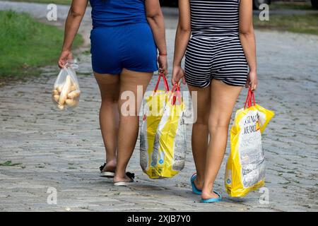 Due donne che camminano su un sentiero acciottolato trasportando sacchetti gialli e un piccolo sacchetto di plastica con rotoli Foto Stock