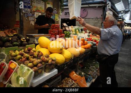 Un uomo israeliano che indossa abiti estivi acquista da un venditore di prodotti in un mercato di Machane Yehuda qui vengono venduti fichi, avocado, melone, arance e pomodori ciliegini Foto Stock