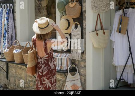 Giovane donna che sceglie un cappello estivo di paglia al negozio di souvenir Foto Stock