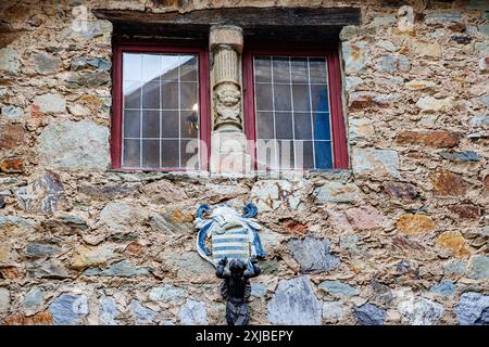 Waimes, Belgio. 2 giugno 2024. Primo piano di un vecchio muro di pietra con una colonna tra due finestre, stemma e sculture decorative a Reinhardstei Foto Stock