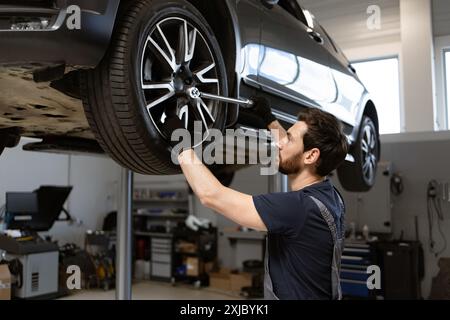 Meccanico che lavora su uno pneumatico di un'auto sopraelevata in un'officina di riparazione auto Foto Stock