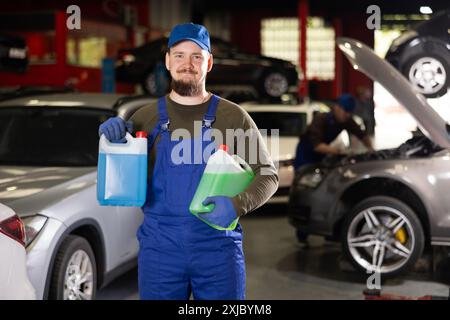 Ritratto di un meccanico professionista in uniforme con bombole di antigelo blu e rosso nelle mani Foto Stock