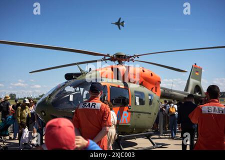 Il pubblico e il personale intorno a un elicottero di salvataggio Airbus H-145 SAR LUH assistono a uno spettacolo aereo di un aereo da caccia Panavia PA-200 Tornado, ILA Berlin 2024. Foto Stock