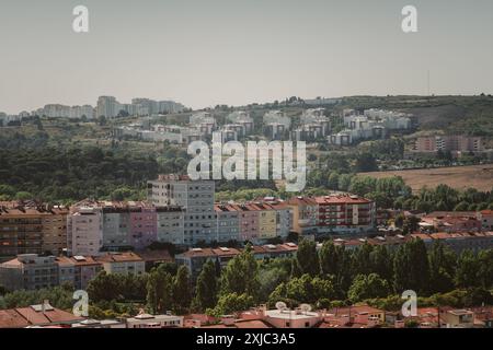 Un'area suburbana vicino a Lisbona caratterizzata da colorati edifici residenziali in primo piano e da blocchi di appartamenti densamente affollati su una collina nel retro Foto Stock