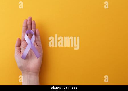 Donna con nastro di sensibilizzazione viola su sfondo arancione, vista dall'alto. Spazio per il testo Foto Stock