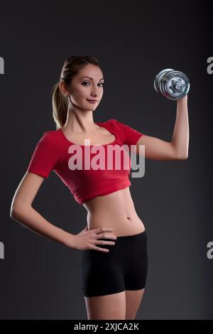 Una donna orgogliosa solleva pesi in palestra, trasudando fiducia e determinazione, mostrando la sua forza e il suo corpo tonificato con un sorriso felice, incarnando un hea Foto Stock