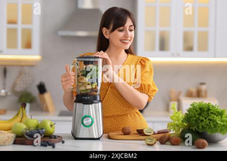 Giovane donna che prepara deliziosi frullati con frullatore al tavolo di marmo bianco in cucina Foto Stock