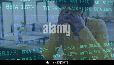 Immagine di un trading board multicolore su una donna afroamericana stanca che lavora su un laptop Foto Stock