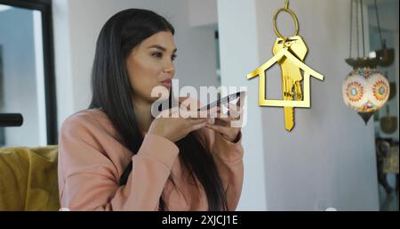 Immagine della chiave della casa d'oro e del telecomando sopra una donna birazziale felice che usa lo smartphone a casa Foto Stock