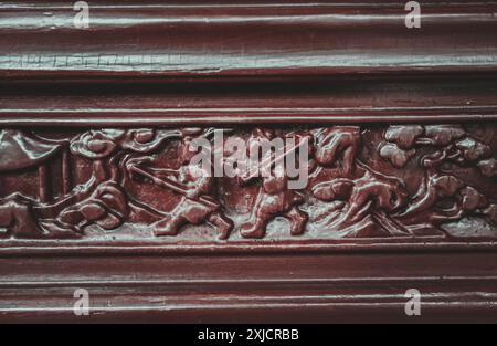 Intricato design in legno intagliato con figure in rilievo all'esterno di una struttura in legno rosso. Foto Stock