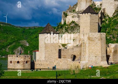 La Fortezza Golubac si erge orgogliosamente su uno sfondo di lussureggiante vegetazione e turbine eoliche, sotto un cielo blu vibrante punteggiato di nuvole Foto Stock