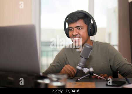 Questo iamge è incentrato sull'uomo che indossa cuffie alla scrivania con laptop e microfono Foto Stock