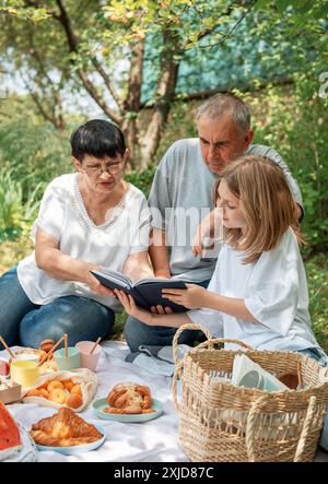 La famiglia trascorre del tempo insieme a un picnic. Nonni e nipoti che leggono un libro durante un picnic estivo Foto Stock