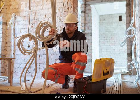 Appaltatore elettrico maschio che lavora con più cavi durante l'installazione precess in cantiere. Foto Stock