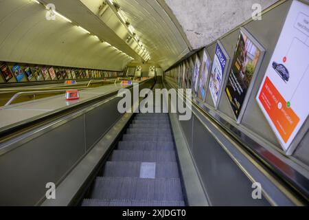 Una scala mobile vuota che scende verso una stazione della metropolitana di Londra, vuota, argentata, isolata Foto Stock