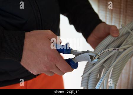 Primo piano di mani elettriciste maschili che tengono tagliafili e tagliano filo bianco. Foto Stock