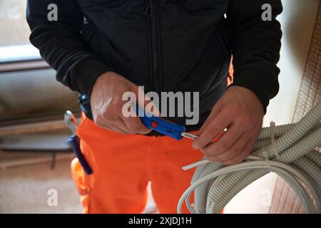 Primo piano di mani elettriciste maschili che tengono tagliafili e tagliano filo bianco. Foto Stock