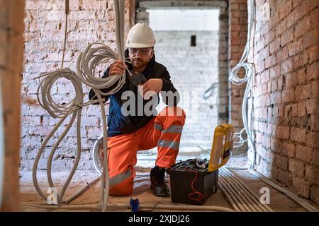 Appaltatore elettrico maschio che lavora con più cavi durante il processo di installazione in cantiere. Foto Stock