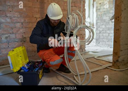 Appaltatore elettrico maschio che lavora con più cavi durante l'installazione precess in cantiere. Foto Stock