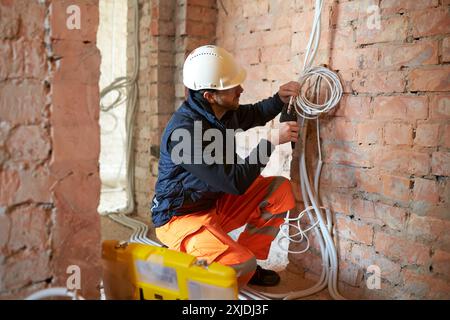 Appaltatore elettrico maschio che lavora con più cavi durante l'installazione precess in cantiere. Foto Stock