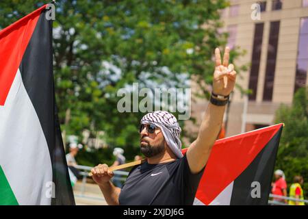 Milwaukee, Stati Uniti. 15 luglio 2024. Un manifestante fa un segno di pace mentre tiene una bandiera palestinese durante una manifestazione contro l'ex presidente Donald Trump al di fuori del Finserv Forum il primo giorno della Convenzione Nazionale Repubblicana (RNC) a Milwaukee, Wisconsin. La convenzione va avanti come previsto nonostante il tentativo di assassinio contro Trump si concluderà con lui accettando la nomina presidenziale del suo partito. Credito: SOPA Images Limited/Alamy Live News Foto Stock