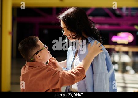 Una madre e un figlio con la sindrome di Down condividono un momento di amore mentre camminano attraverso un centro commerciale. Foto Stock