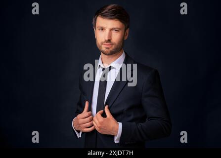 Uomo in tuta che regola la cravatta su sfondo scuro Foto Stock