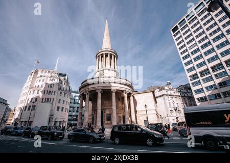 Londra, Regno Unito - 10 ottobre 2023: Una guglia della chiesa sbircia sopra le vivaci strade di Londra, Regno Unito. Le auto navigano dietro l'angolo di Regent Street, incl Foto Stock