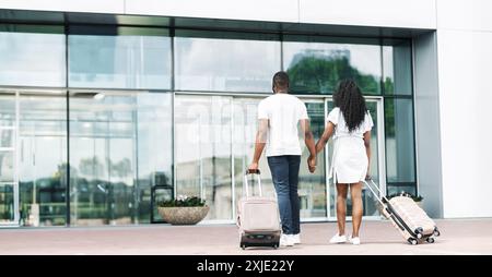 Coppia a piedi dall'ingresso dell'aeroporto con bagagli, vista posteriore Foto Stock
