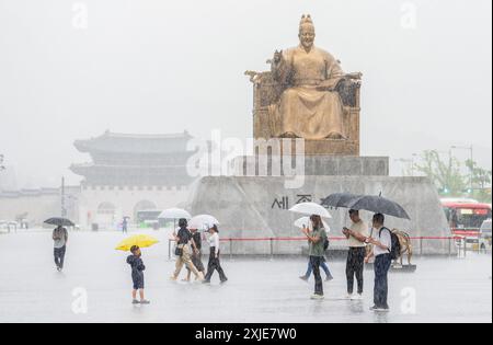 Seoul, Corea del Sud. 18 luglio 2024. Le persone che hanno degli ombrelli per proteggersi dalla pioggia camminano attraverso una statua di Sejong il grande nella piazza centrale di Gwanghwamun a Seoul. Il 18 luglio, i torrenziali hanno toccato la più ampia area di Seoul e le regioni adiacenti, portando all'evacuazione dei residenti a causa dei corsi d'acqua gonfiati e della chiusura delle autostrade, un ponte a Seoul e i vicini servizi della metropolitana. Credito: SOPA Images Limited/Alamy Live News Foto Stock