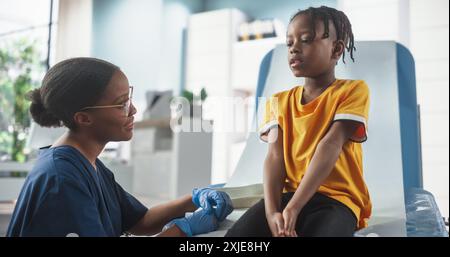 Ragazzo africano seduto sulla sedia in ospedale, parlando con infermiera nera femminile. Donna professionale che ascolta i sintomi di Young Man, dà consigli su un trattamento adeguato. Concetto di sanità pubblica. Foto Stock