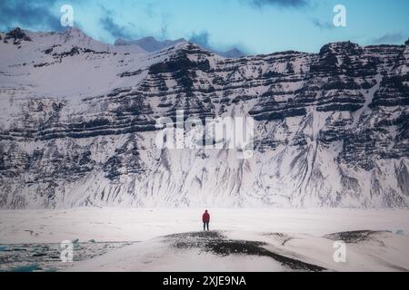 Escursionista solitario di fronte a una massiccia catena montuosa durante l'inverno in Islanda, sul sentiero, viaggiatore, escursionismo maschile da solo, turista Foto Stock