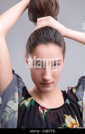 Giovane donna elegante con capelli marroni e naso che perforano con sicurezza la fotocamera. Sfoggia un'espressione unica di sé in una camicia floreale con i capelli su e. Foto Stock