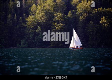 I turisti a bordo di una piccola barca a vela prima del tramonto sullo spettacolare lago di Bohinj nel parco nazionale del Triglav in Slovenia Foto Stock