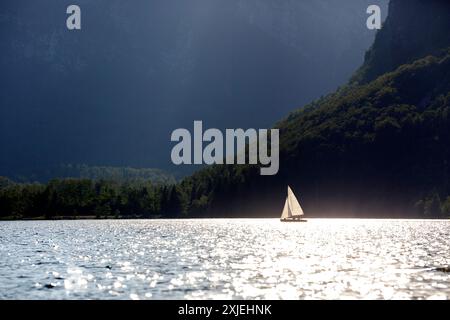 I turisti a bordo di una piccola barca a vela prima del tramonto sullo spettacolare lago di Bohinj nel parco nazionale del Triglav in Slovenia Foto Stock