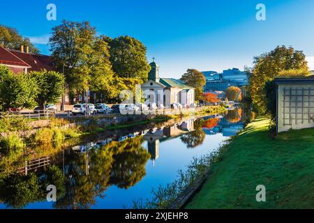 Le acque calme di un canale riflettono l'edificio di una chiesa a Goteborg, Svezia. L'ambiente è idilliaco, con cieli azzurri e alberi verdi. Foto Stock