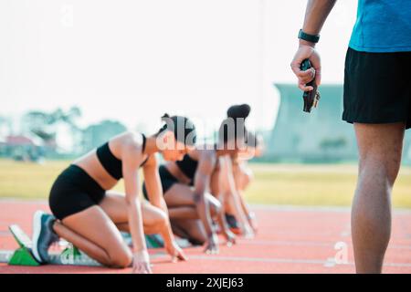 Mano, gara e persona con pistola di avviamento per correre, fare esercizio fisico o maratona in pista. A partire da pistola, gruppo e donne in campo per stadio per prepararsi Foto Stock