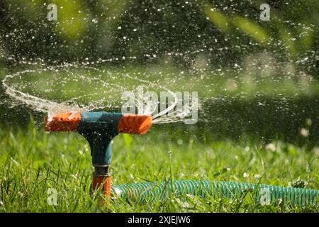 Irrigatore da giardino nelle soleggiate giornate estive durante l'innaffiatura del prato verde in giardino. Sistema di irrigazione intelligente automatico. Primo piano. Foto Stock